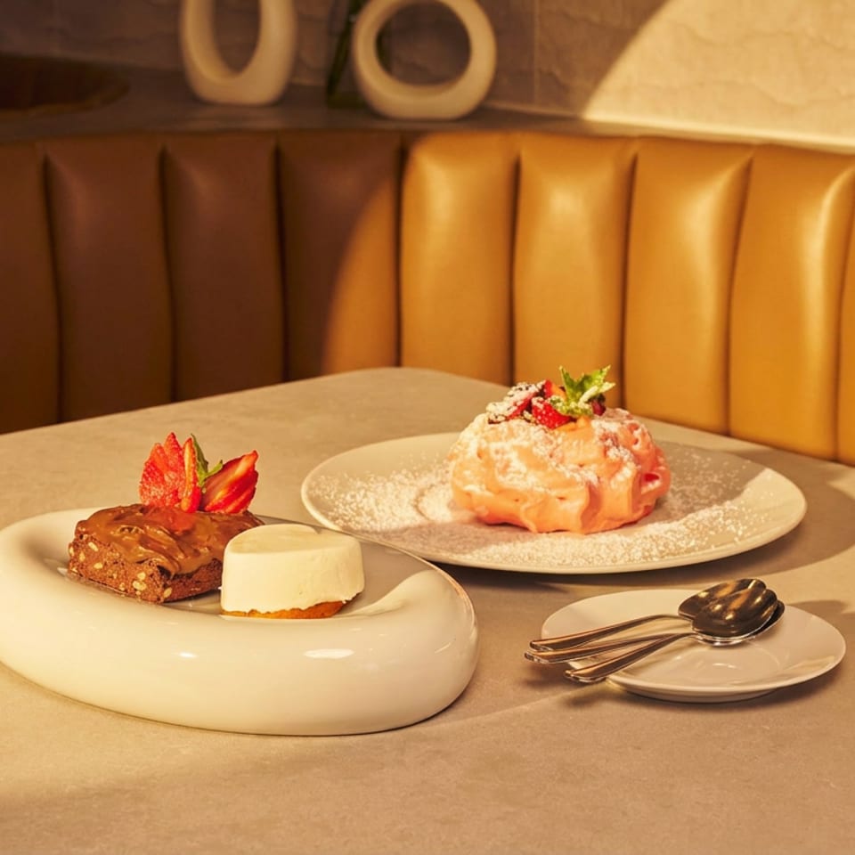 Elegant restaurant table with plated pastries, strawberries, powdered sugar, and silverware against a warm leather booth.