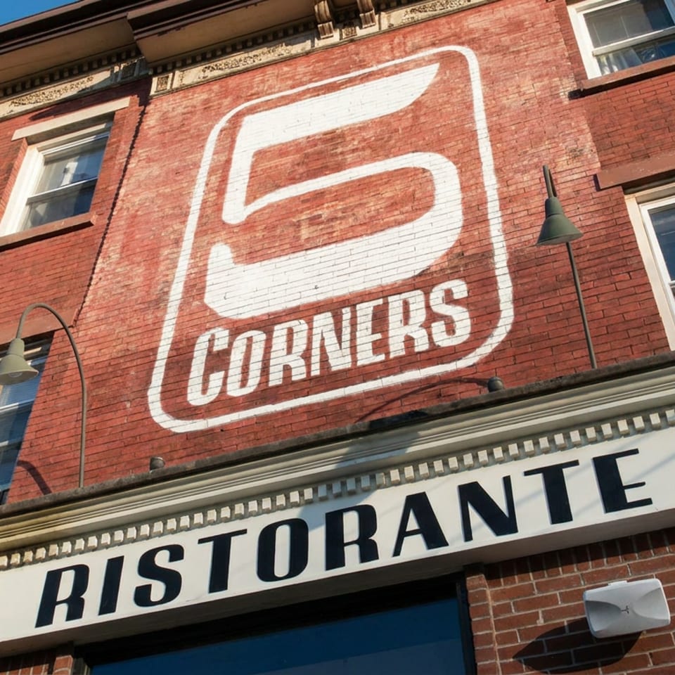 Red brick restaurant facade with large Corners logo, Bistro sign, windows, and curved exterior lamps under a blue sky.